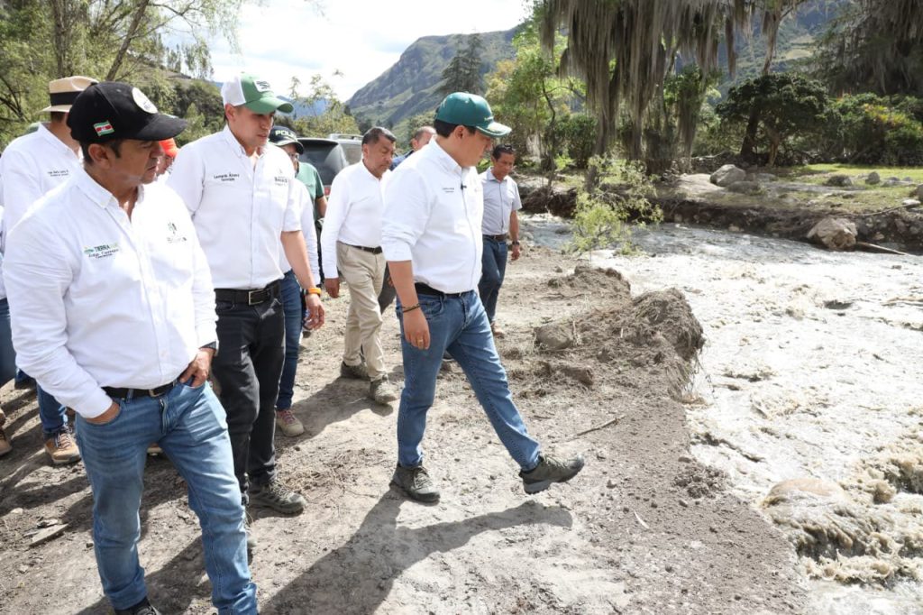 Funcionarios con camisas de la Gobernación recorren la orilla de un río crecido durante la emergencia invernal en Boyacá