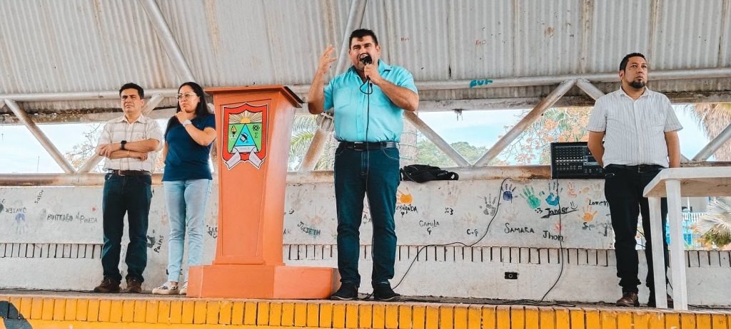 San Luis de Gaceno en febrero de 2026: un hombre habla por micrófono junto a un atril naranja con el escudo de la IE San Luis de Gaceno, acompañado por tres personas en la tarima