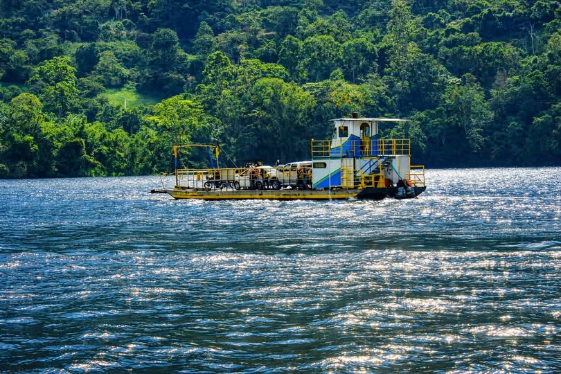 Planchón con vehículos a bordo cruza el embalse La Esmeralda, frente a una montaña cubierta de vegetación