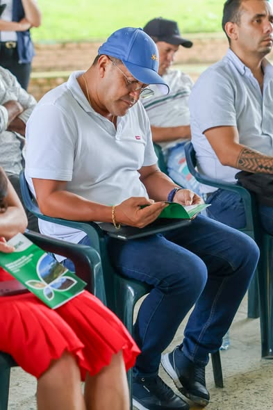 Asistentes sentados en sillas plásticas leen un folleto verde durante la socialización del plan de riesgo del Campo Medina en Horizontes