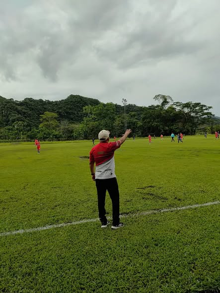 Un hombre con gorra da indicaciones desde la línea durante un partido de fútbol en una cancha de césped