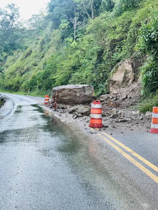 Roca de gran tamaño y material de derrumbe sobre un carril de la Transversal del Sisga, señalizado con barriles