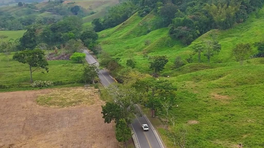 Vista aérea de la Transversal del Sisga entre montañas verdes, con una camioneta blanca en la vía