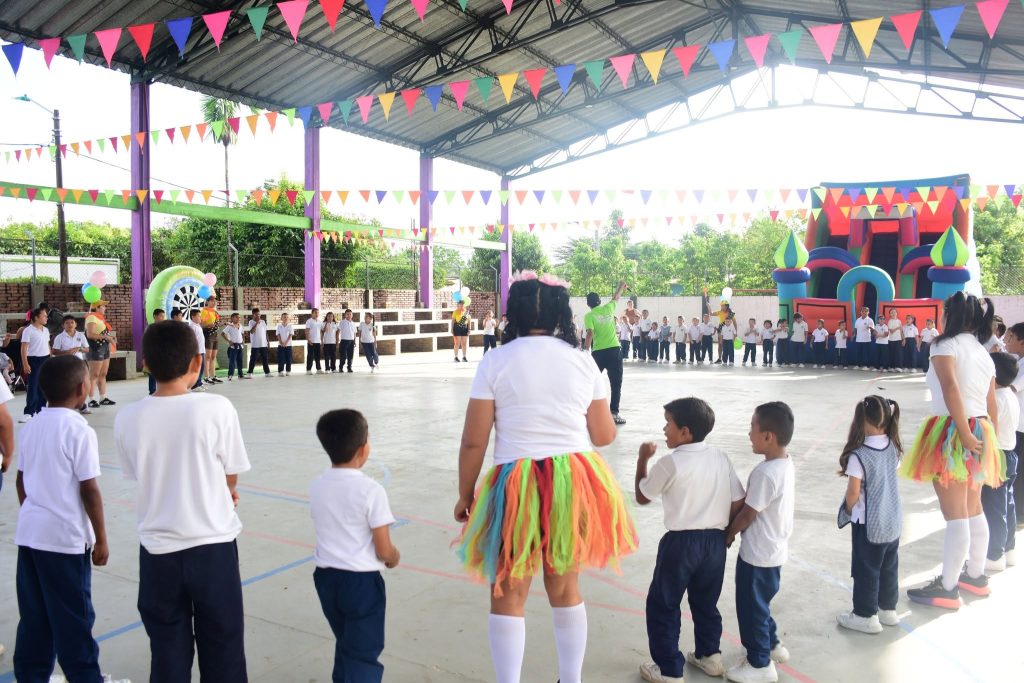 Niños de uniforme escolar en una cancha cubierta con banderines y un inflable por el Día de las Niñas y los Niños en Sabanalarga