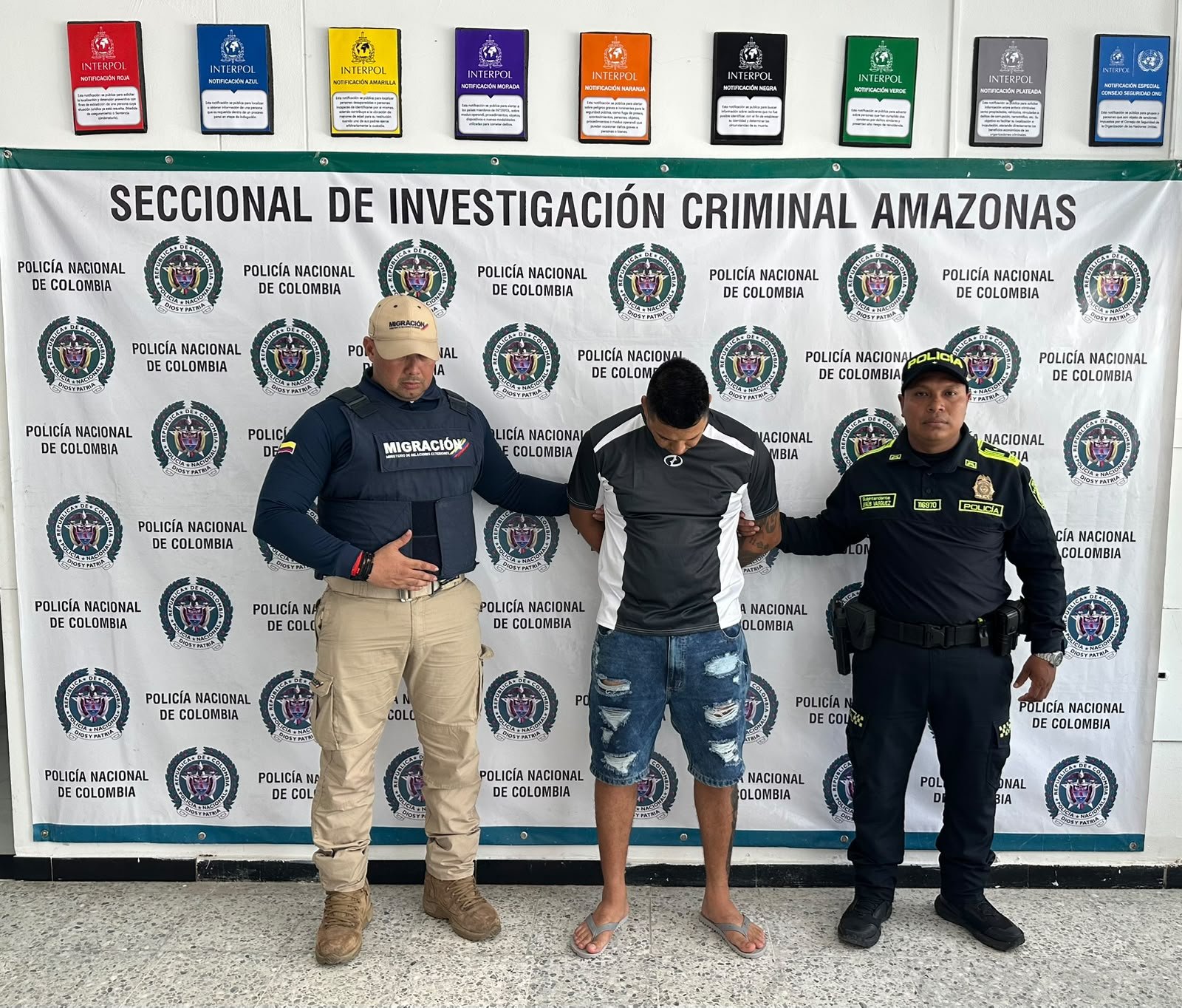 Alias Giovanny junto a uniformados frente al pendón de la Seccional de Investigación Criminal de Amazonas