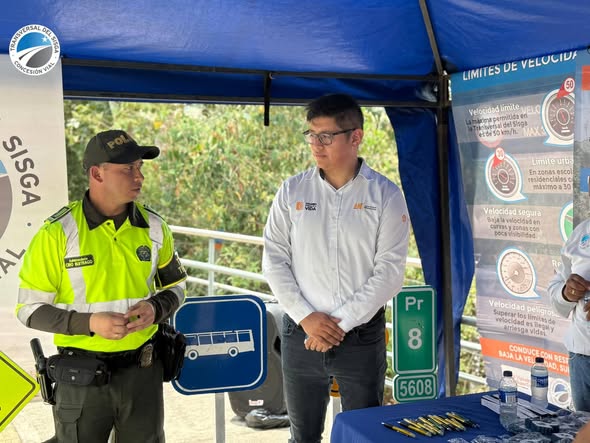 Policía de tránsito y funcionario de la concesión junto a un cartel de límites de velocidad en Sabanalarga