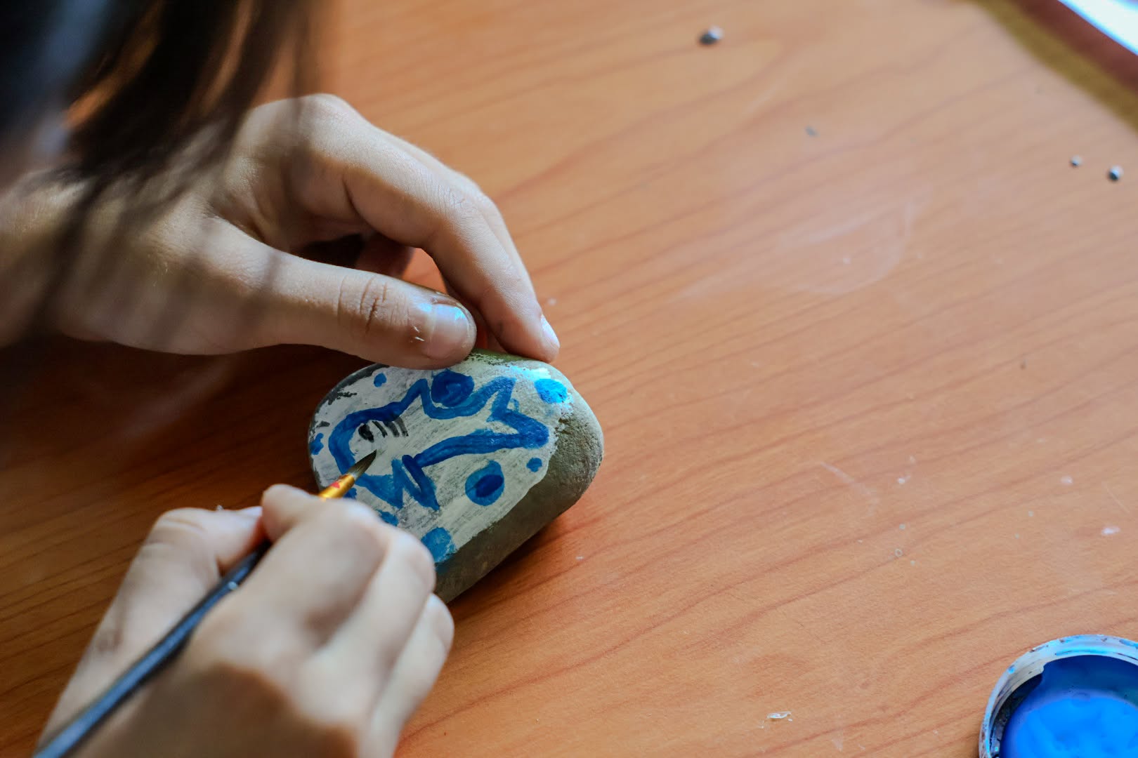 Manos de una niña pintan una piedra de azul en el martes de pintura de la Biblioteca de San Luis de Gaceno