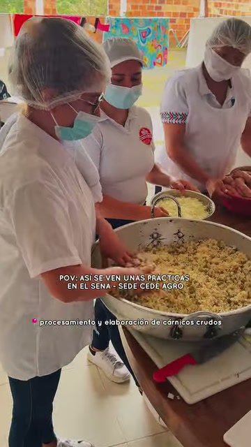 Tres aprendices del SENA con cofia y tapabocas mezclan ingredientes en un recipiente metálico