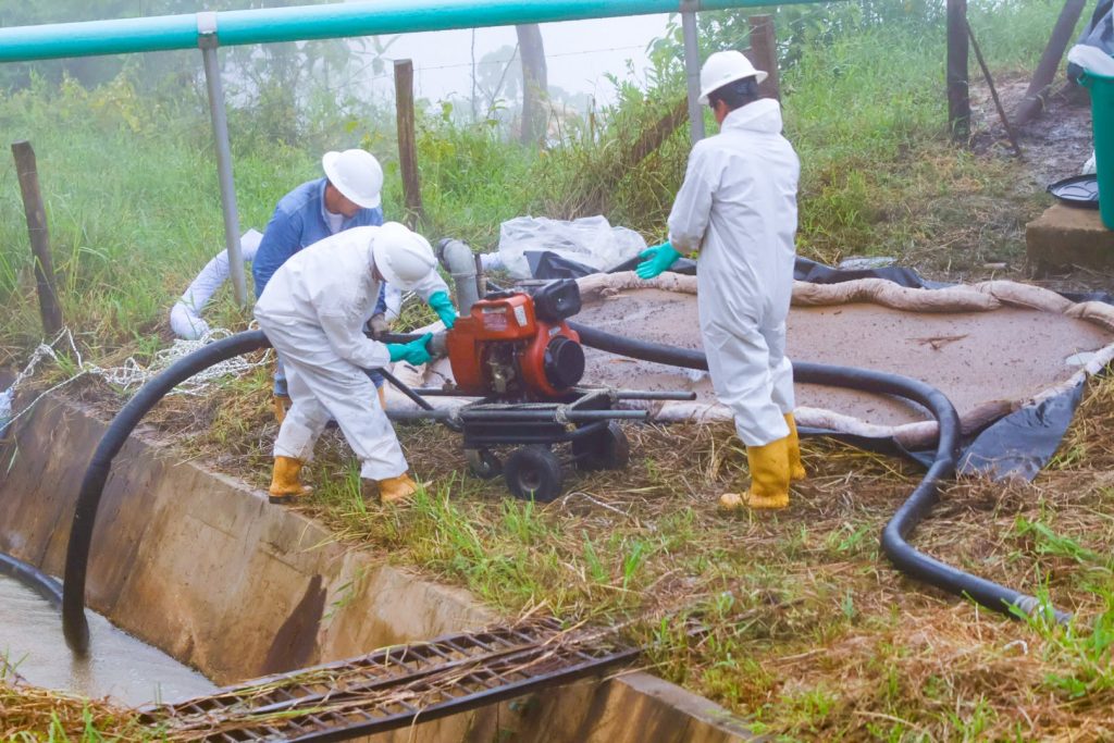 Simulacro del Campo Medina en Horizontes: operarios con trajes blancos manejan una motobomba junto a un canal